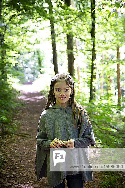 Portrait of smiling girl standing on hiking trail against trees in forest