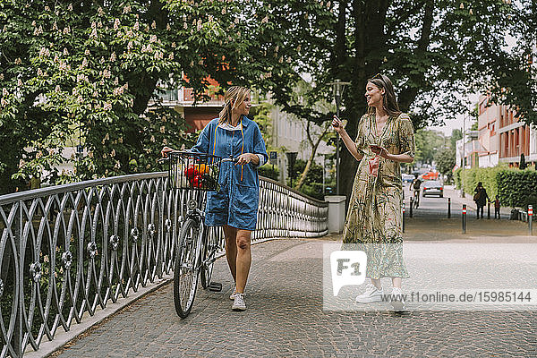 Zwei Frauen mit Fahrrad und Gesichtsmaske gehen auf einer Brücke