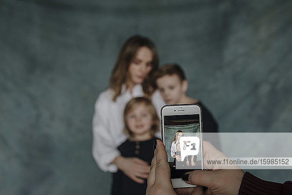 Hand einer Frau  die ihre Familie zu Hause mit dem Smartphone fotografiert
