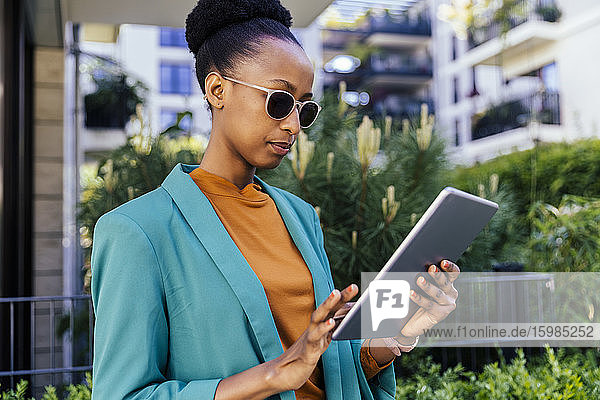 Porträt einer jungen Geschäftsfrau mit Sonnenbrille  die im Freien ein digitales Tablet benutzt