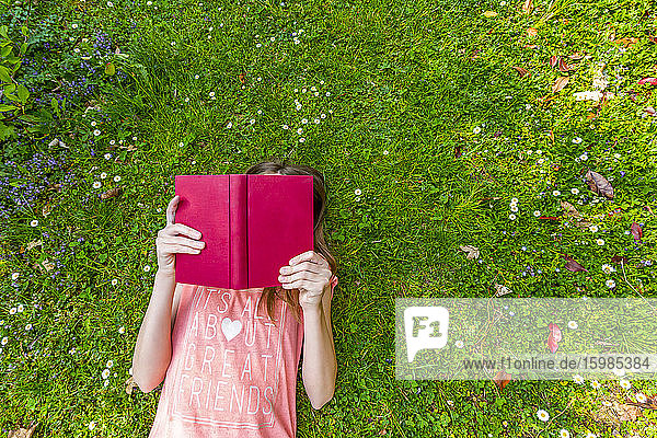 Mädchen liegt auf einer Wiese und liest ein Buch  Ansicht von oben