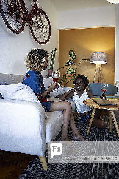Zwei Frauen trinken ein Glas Wein und unterhalten sich im Wohnzimmer