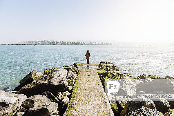 Full length rear view of woman standing on pier while looking at sea against clear sky during sunny day
