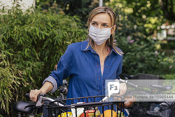 Frau mit Gesichtsmaske  die mit dem Fahrrad in der Stadt Lebensmittel einkaufte