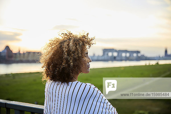 Rückansicht einer Frau  die die Aussicht von der Brücke im Abendlicht genießt