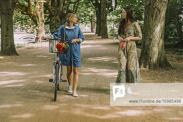 Zwei Frauen mit Fahrrad und Gesichtsmaske gehen im Park spazieren