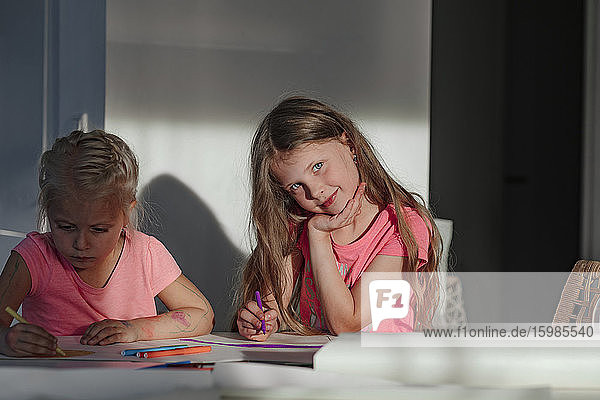 Glückliches Mädchen  das mit seiner Schwester sitzt und zu Hause auf Papier malt