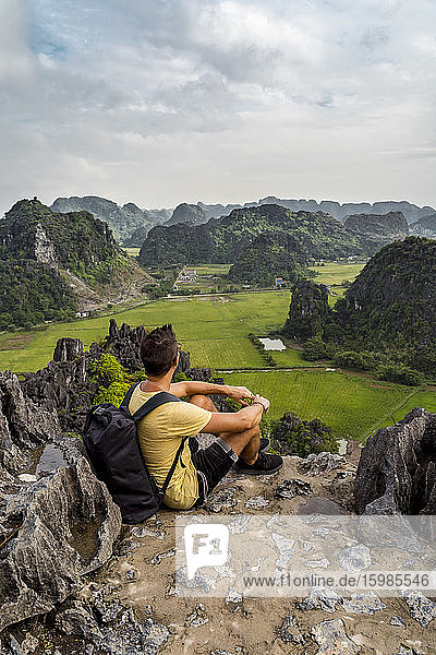Vietnam  Ninh Binh Province  Ninh Binh  Male hiker admiring scenic landscape of Hong River Delta from top of karst formation