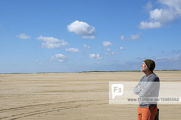 Thoughtful mature man standing at beach against blue sky on sunny day