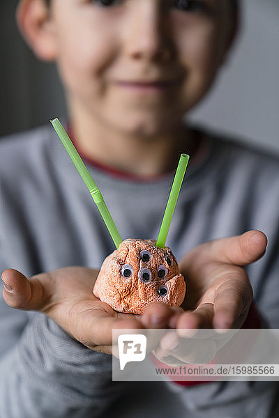 Close-up of boy holding toy alien made from clay and straw at home