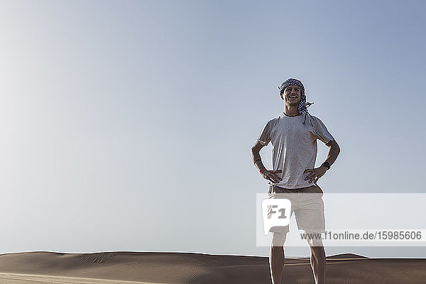 Smiling tourist standing with hands on hip against clear sky at desert in Dubai United Arab Emirates