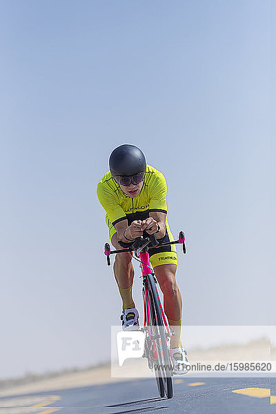 Entschlossener männlicher Radfahrer  der auf der Straße in der Wüste Fahrrad fährt  Dubai  Vereinigte Arabische Emirate