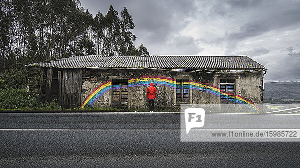 Spain  Province of A Coruna  San Saturnino  Man looking at rainbow painted on abandoned roadside house