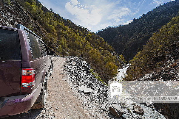 Georgia  Svaneti  Ushguli  4x4 car driving along mountain road overlooking river flowing along forested valley