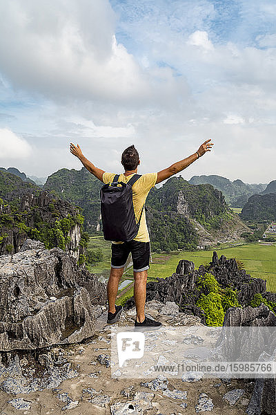 Vietnam  Ninh Binh Province  Ninh Binh  Male hiker standing with raised arms at edge of Hong River Delta karst formation