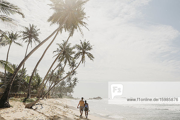 Rear view of romantic couple walking on sea shore at beach against sky  Sri Lanka
