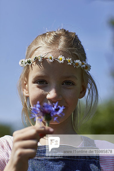 Porträt eines Mädchens  das einen Gänseblümchenkranz trägt und eine Blume hält