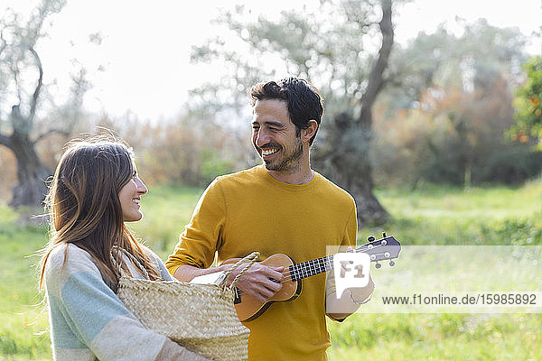 Woman carrying wicker basket while happy man playing guitar at countryside