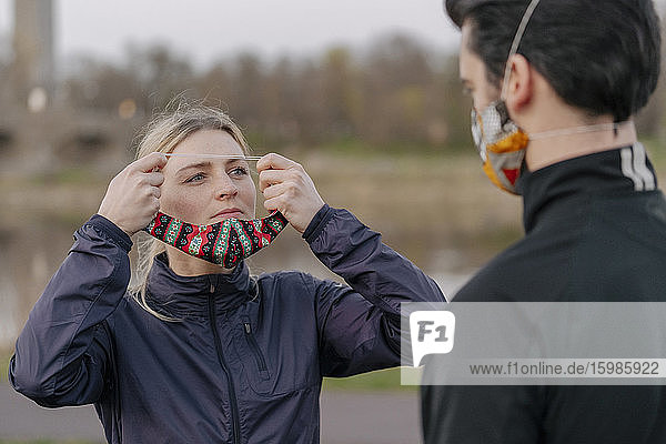 Frau schaut Mann an  während sie im Park eine Gesichtsmaske trägt
