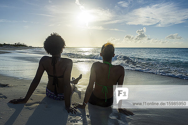 Rückansicht von Freundinnen  die bei Sonnenuntergang am Strand von Grace Bay auf das Meer blicken  Providenciales  Turks- und Caicosinseln