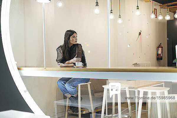 Schöne Frau in voller Länge  die wegschaut  während sie in einem beleuchteten Cafe sitzt und wartet