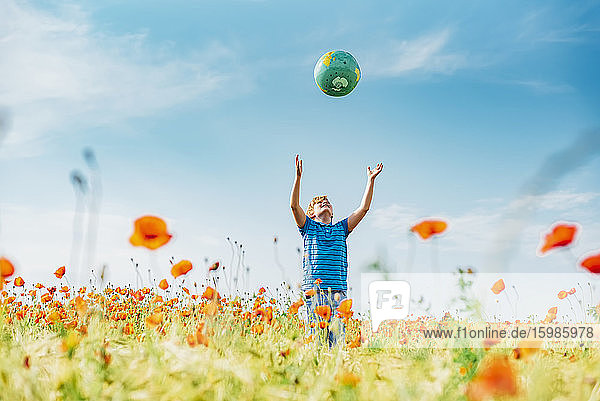 Boy catching globe while standing in poppy field against blue sky on sunny day