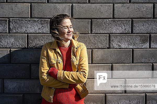 Lächelnde Frau  die an einer Backsteinmauer steht und mit Kopfhörern Musik hört