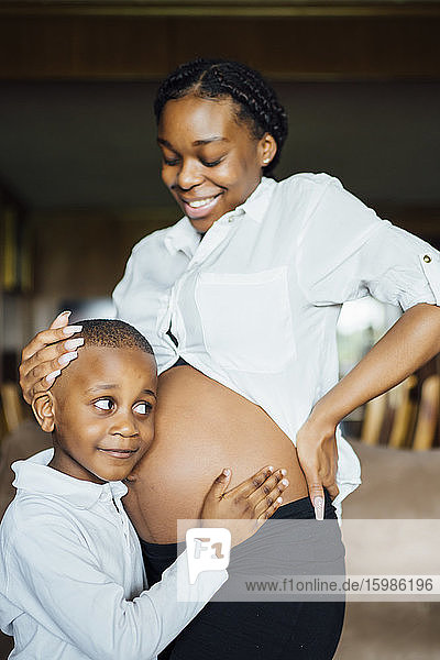 Kleiner Junge lauscht am Bauch einer schwangeren jungen Frau