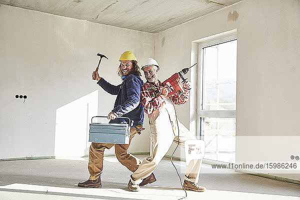 Lächelnde Bauarbeiter mit Bohrmaschine und Werkzeugkasten auf der Baustelle