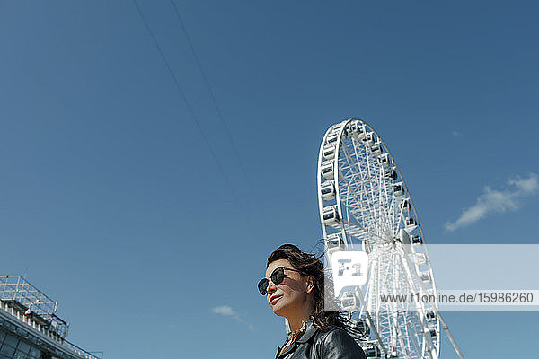 Woman wearing sunglasses near Ferris wheel against blue sky