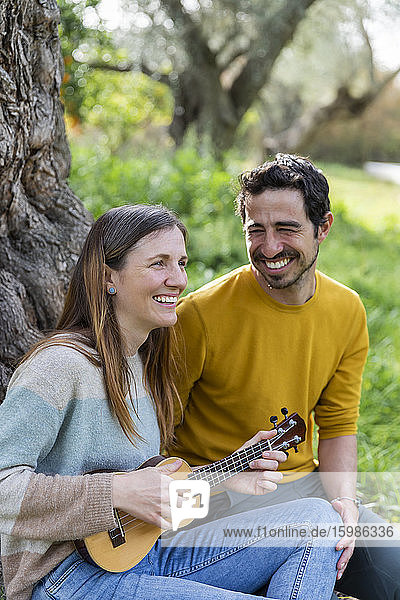 Fröhlicher Mann  der seine Freundin beim Gitarrenspiel beobachtet  während er auf dem Lande sitzt