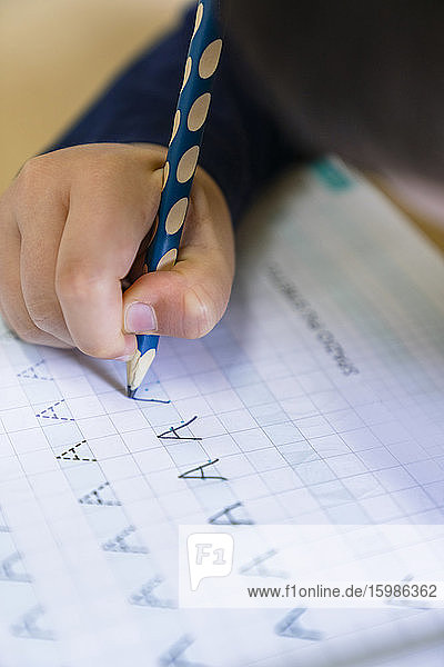 Hand eines Jungen  der zu Hause mit einem Bleistift den Buchstaben A auf Papier schreibt