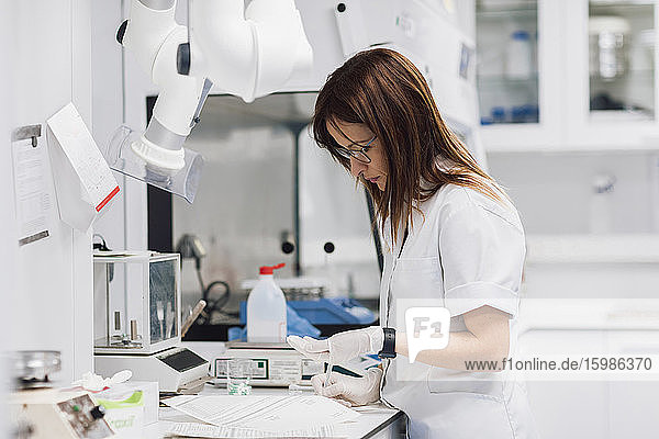Reife Pharmazeutin hält Tabletten in der Hand  während sie an einem Schreibtisch im Labor steht