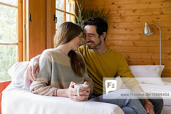 Smiling couple romancing while sitting on sofa in log cabin