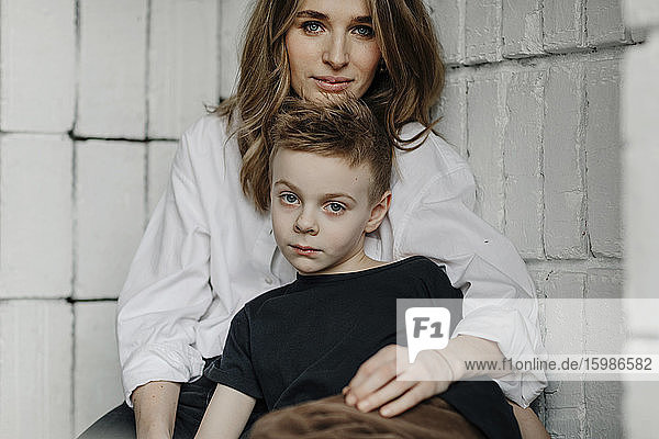 Portrait of confident mother with son sitting on niche at home