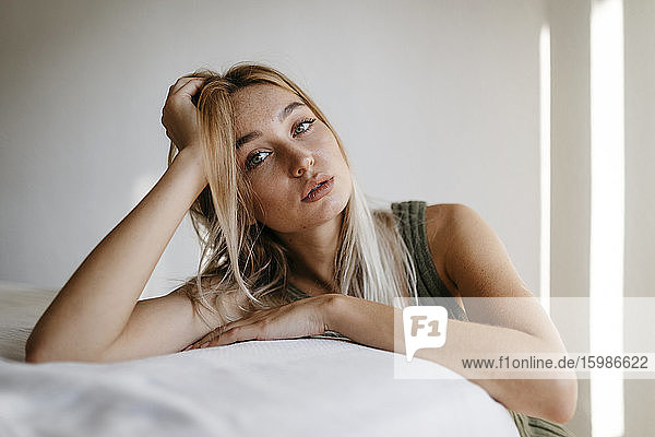 Verführerische junge Frau mit Hand im Haar lehnt Bett zu Hause