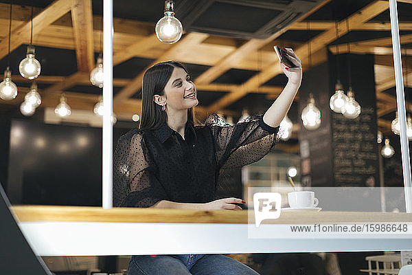 Glückliche junge Frau  die ein Selfie mit ihrem Smartphone macht  während sie in einem Café sitzt