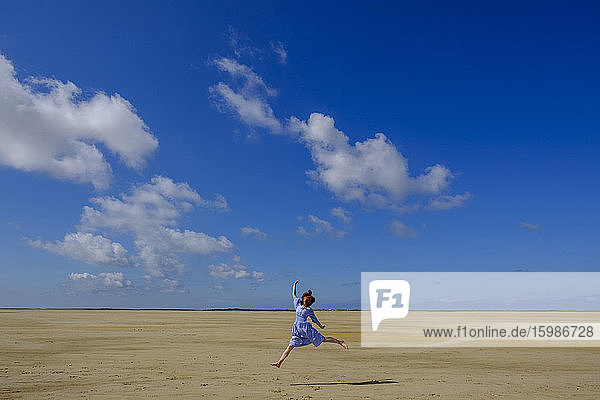In voller Länge von Teenager-Mädchen springen am Strand gegen blauen Himmel an einem sonnigen Tag