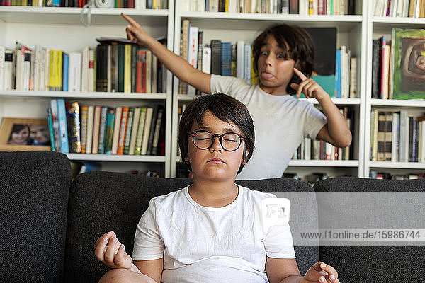 Boy sitting on couch meditating  his brother teasing him