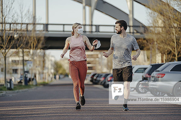 Junge Frau joggt  während sie einem Mann während der COVID-19-Pandemie eine Gesichtsmaske gibt