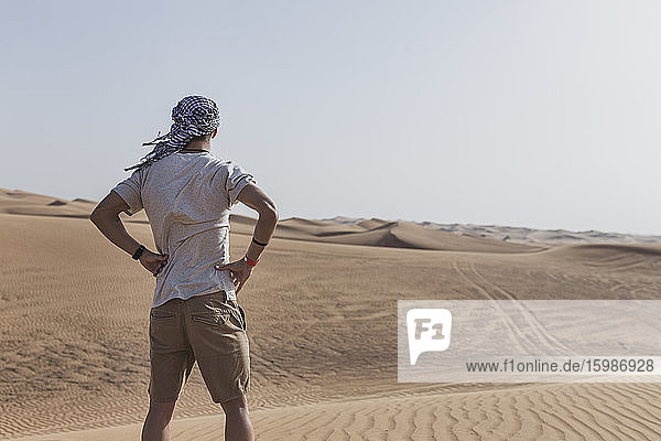 Junger männlicher Tourist steht auf Sanddünen in der Wüste von Dubai  Vereinigte Arabische Emirate