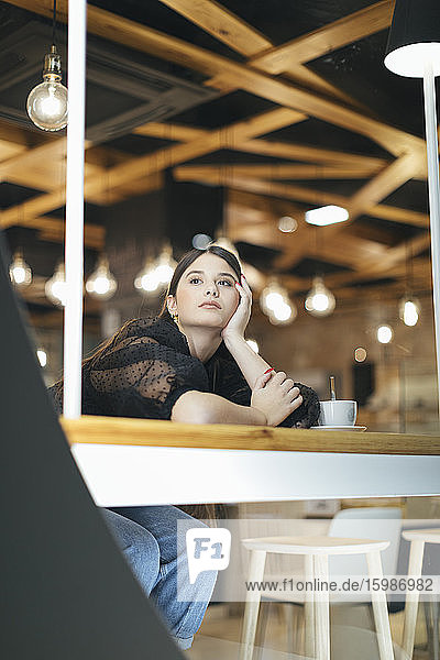 Nachdenkliche junge Frau  die sich auf einen Tisch stützt und in die beleuchtete Cafeteria blickt