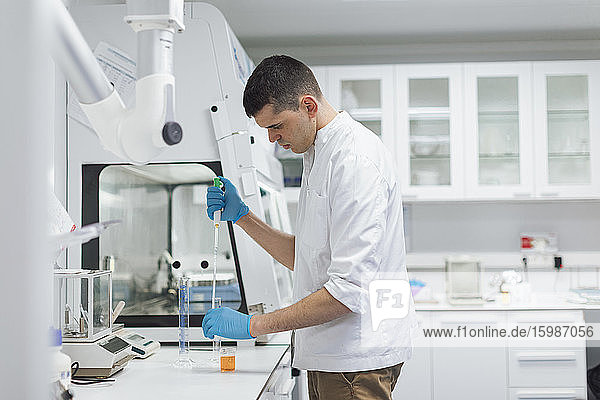Junger männlicher Wissenschaftler  der eine Chemikalie mit einer Pipette aufnimmt  während er im Labor forscht