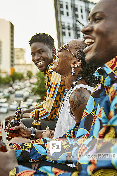 Laughing friends sitting on roof terrace in the city drinking beer  Maputo  Mozambique
