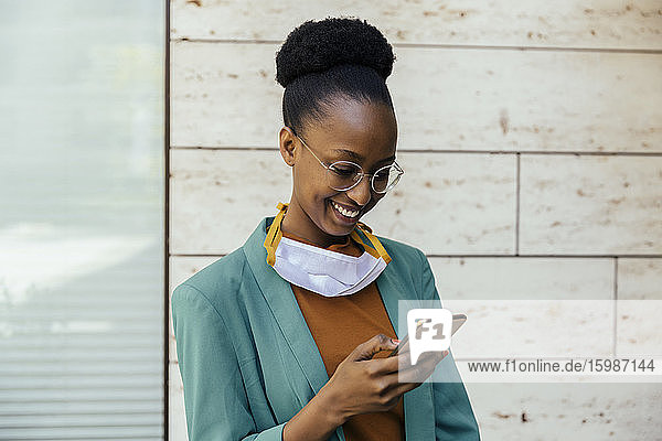 Portrait of smiling businesswoman with protective mask using smartphone