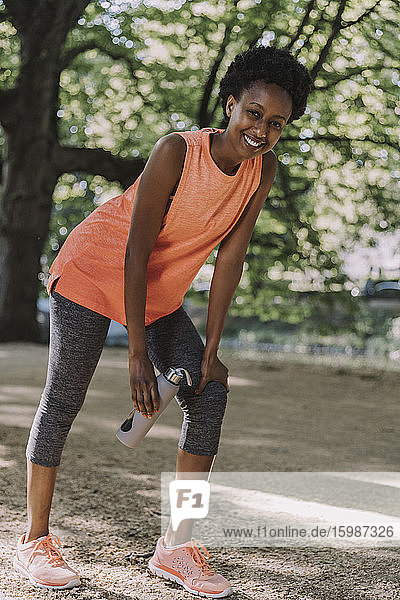 Portrait of smiling young woman taking a break from working out in a park