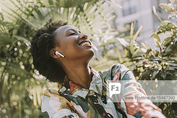 Happy young woman listening music with earphones in garden