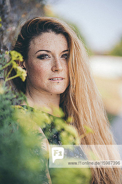 Portrait of beautiful young blond woman with freckles on face standing outdoors