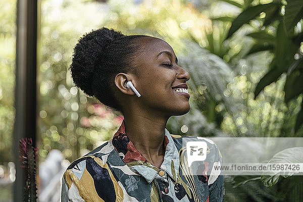 Happy young woman with eyes closed listening music with earphones in garden
