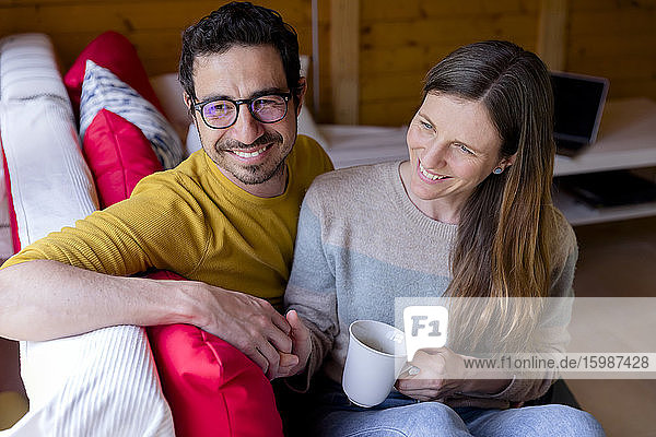 Lächelndes Paar hält sich an den Händen und entspannt sich auf dem Sofa in einer Blockhütte